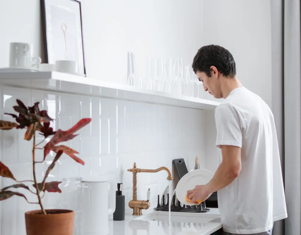 Man washing dishes in a home kitchen, keeping the kitchen tidy to reduce pests